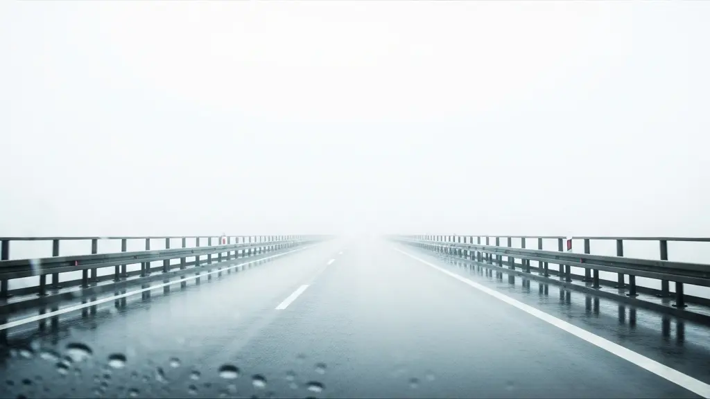 Route d'autoroute disparaissant dans un épais banc de brouillard, surface mouillée reflétant la lumière diffuse, glissières métalliques s'estompant dans la brume